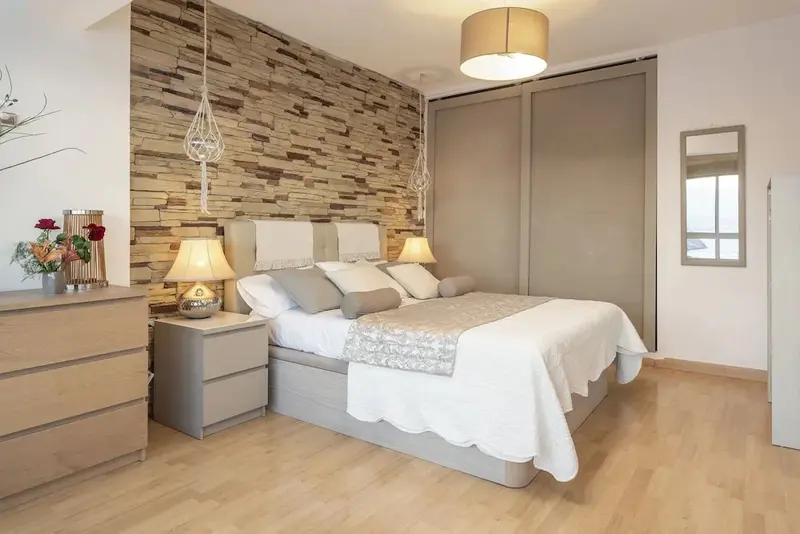 Une chambre lumineuse avec un grand lit et un mur en pierre.