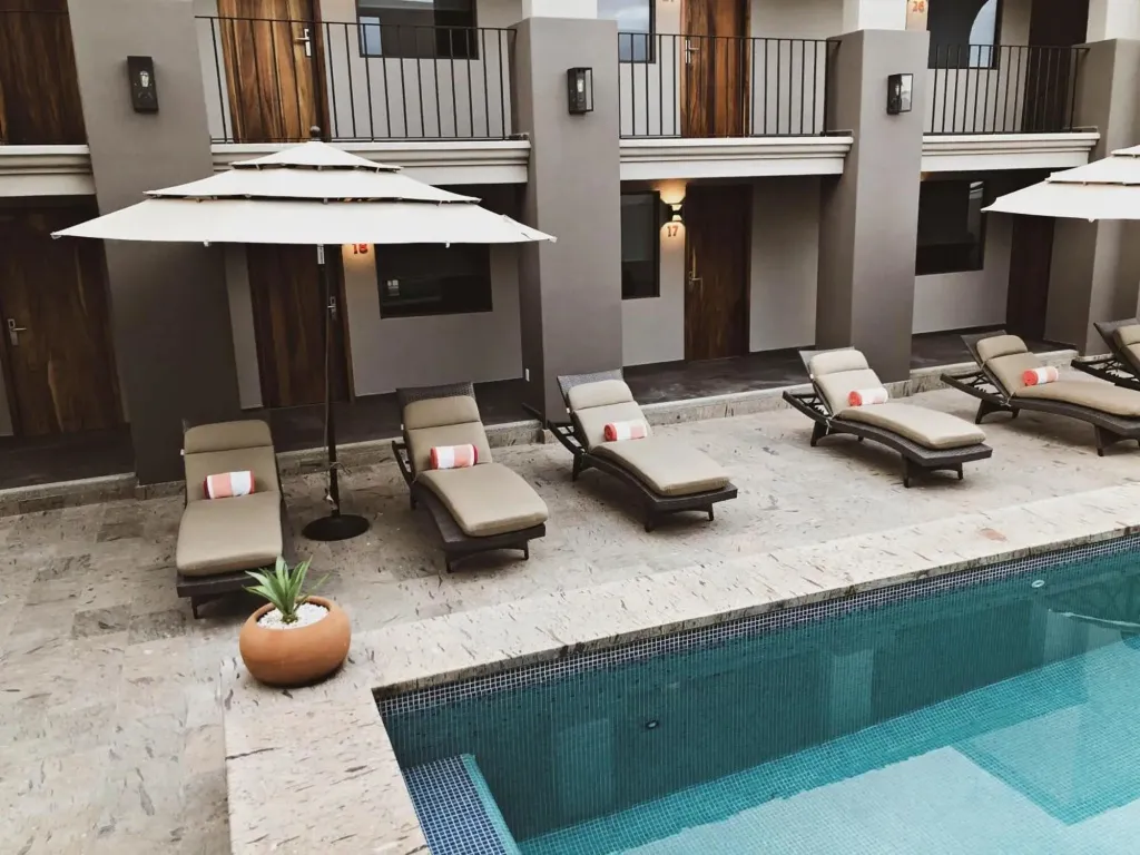 Transats et parasols bordent une piscine rectangulaire dans une cour intérieure.