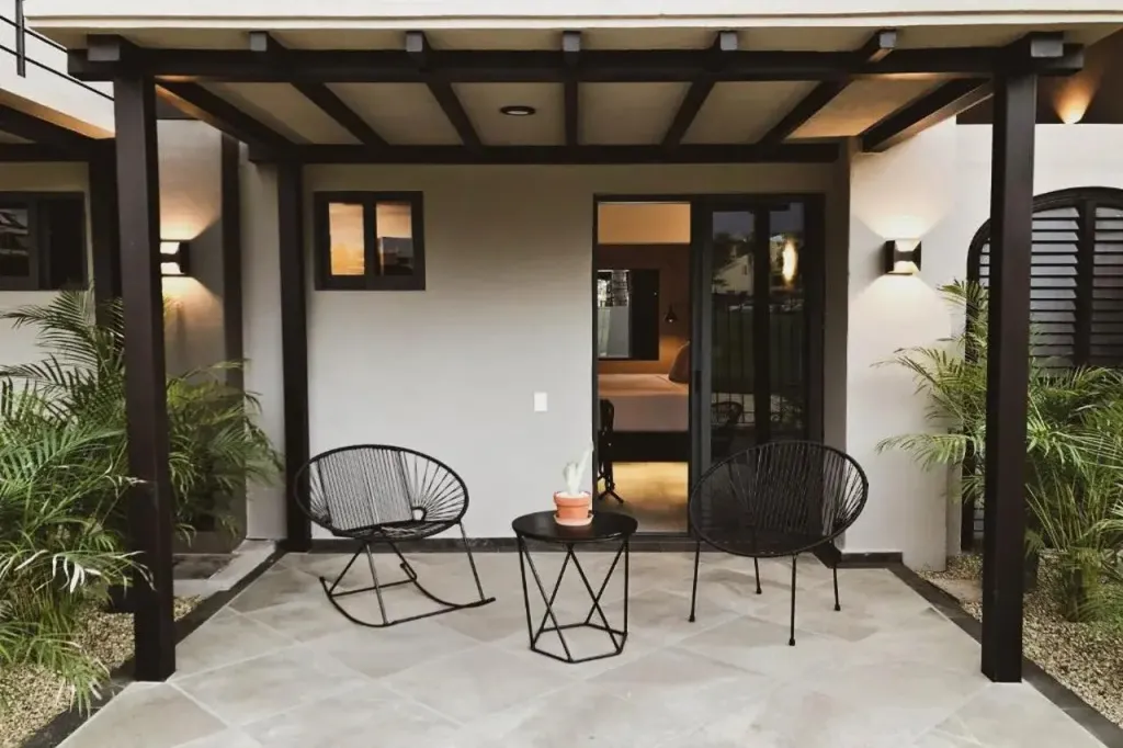 Terrasse ombragée avec mobilier en métal et accès à une chambre.