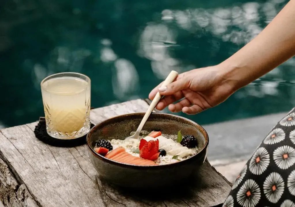 Un bol de fruits frais et une boisson rafraîchissante sont servis sur une table en bois près d'une piscine.