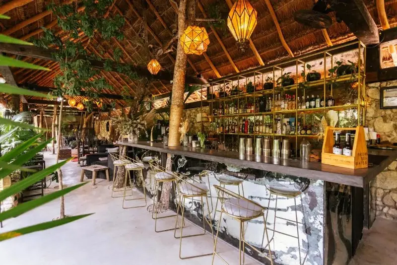 Un bar avec un comptoir en pierre et des tabourets métalliques est éclairé par des lanternes suspendues.