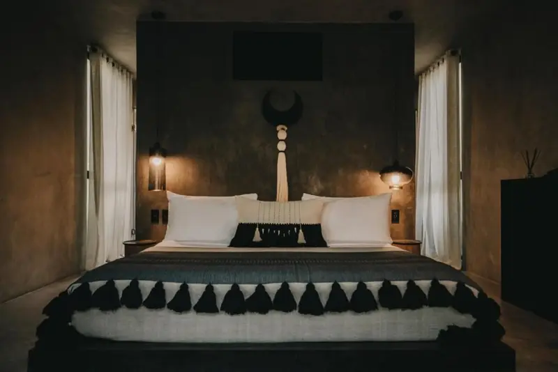 Un lit king-size est dispose dans une chambre aux murs fonces et aux rideaux clairs.