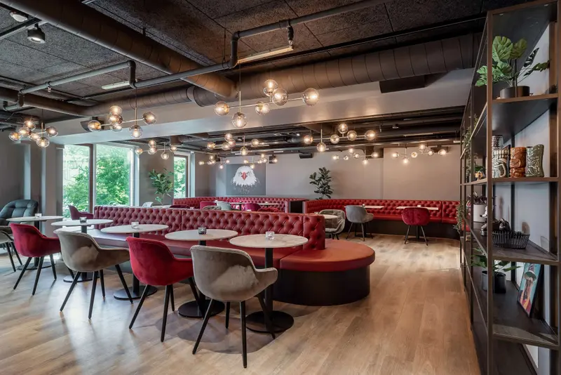 Un espace de restauration moderne avec des banquettes rouges et des tables rondes.