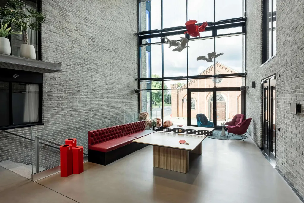 Un espace de détente intérieur avec canapés rouges, une table de ping-pong et de larges baies vitrées.