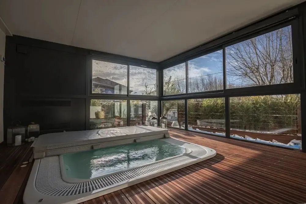Espace de détente intérieur avec jacuzzi et vue sur un jardin à travers de grandes baies vitrées.