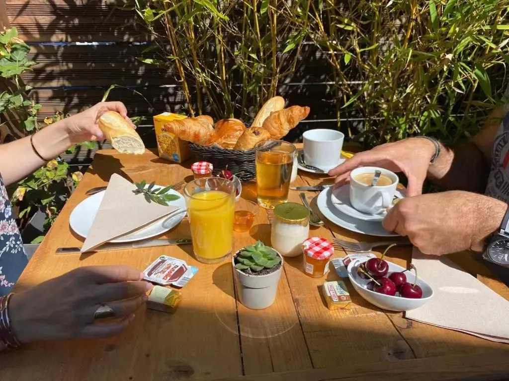 Une table en bois est dressée avec un petit-déjeuner composé de viennoiseries, de jus d'orange et de boissons chaudes.