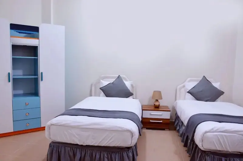Une chambre lumineuse avec deux lits simples et une armoire.