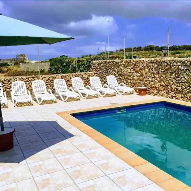 Une piscine rectangulaire bordée de chaises longues sous un parasol.