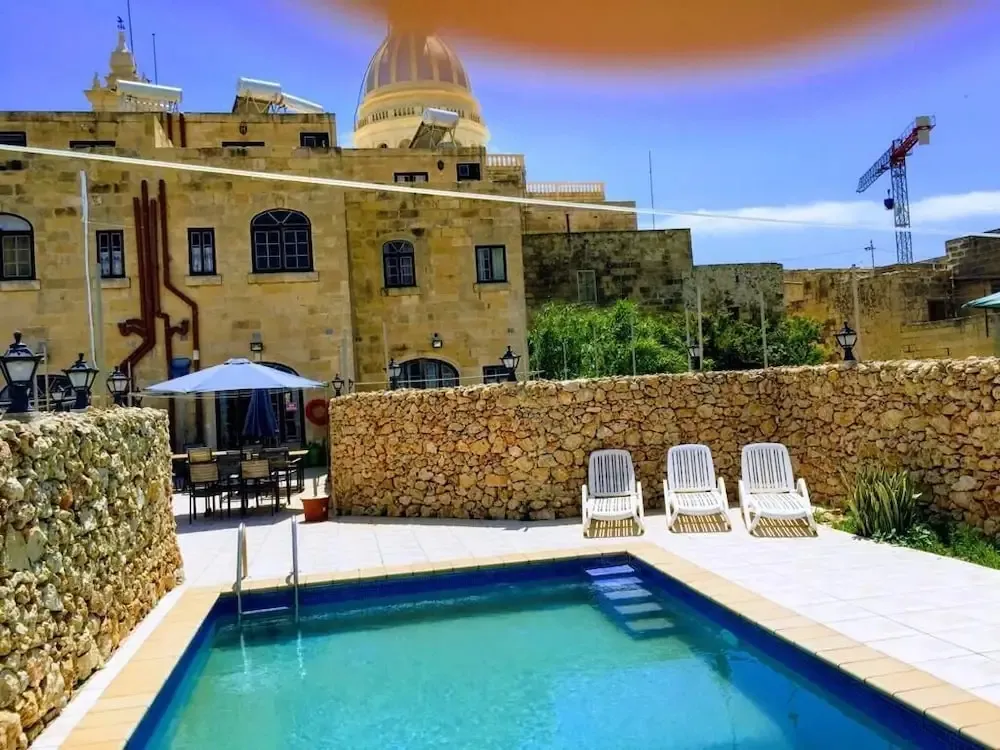 Piscine turquoise devant un bâtiment en pierre claire sous un ciel bleu.