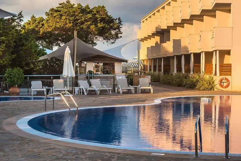 Une piscine au premier plan avec des transats et un bar ombragé à proximité.