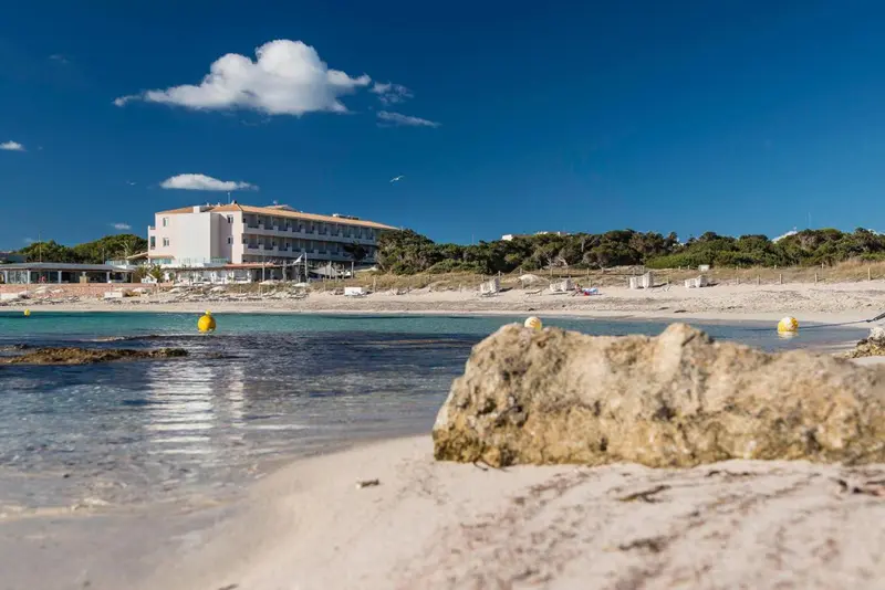 Plage de sable blanc avec eau turquoise et bâtiment en arrière-plan.