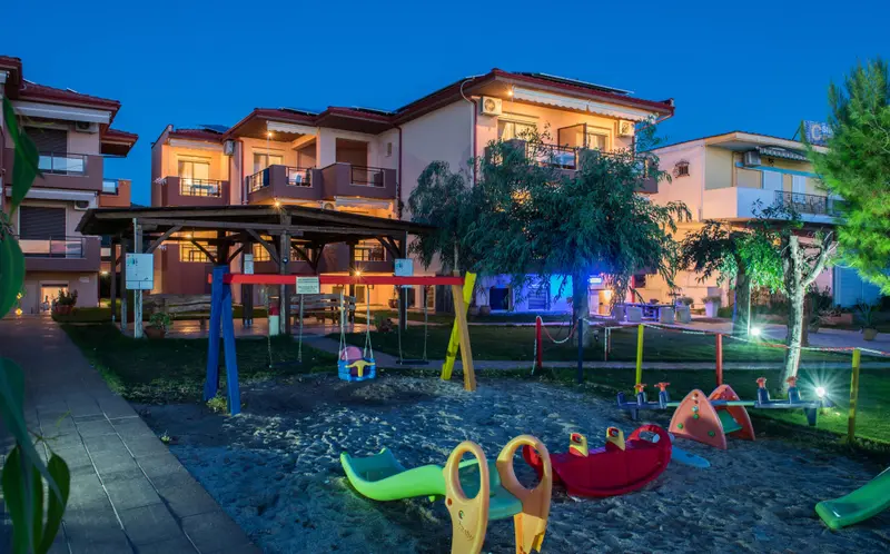 Bâtiment éclairé avec une aire de jeux pour enfants au premier plan.