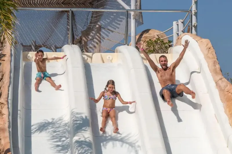 Trois personnes glissent sur des toboggans aquatiques ensoleillés.