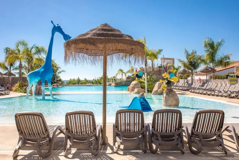 Transats alignés devant une piscine décorée de sculptures colorées sous un ciel bleu.