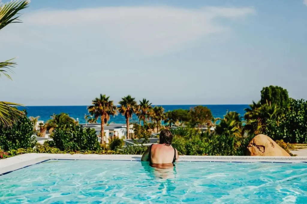 Une personne se détend dans une piscine avec vue sur la mer et la végétation.