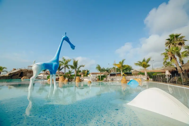 Une piscine turquoise avec une sculpture de girafe bleue au premier plan.