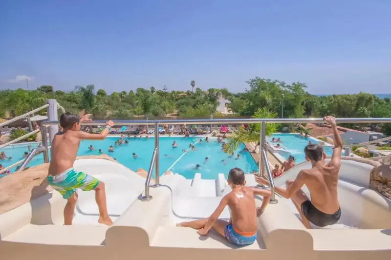 Des adolescents s'apprêtent à glisser sur des toboggans aquatiques dans une piscine ensoleillée.