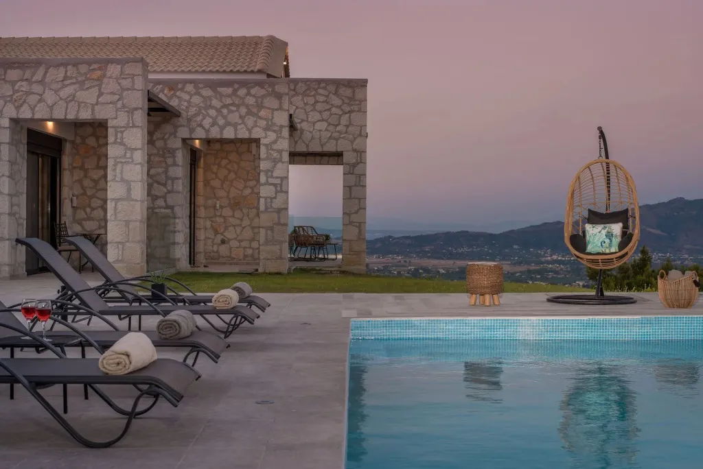 Transats et piscine au bord d'une villa avec vue sur un paysage montagneux au crépuscule.