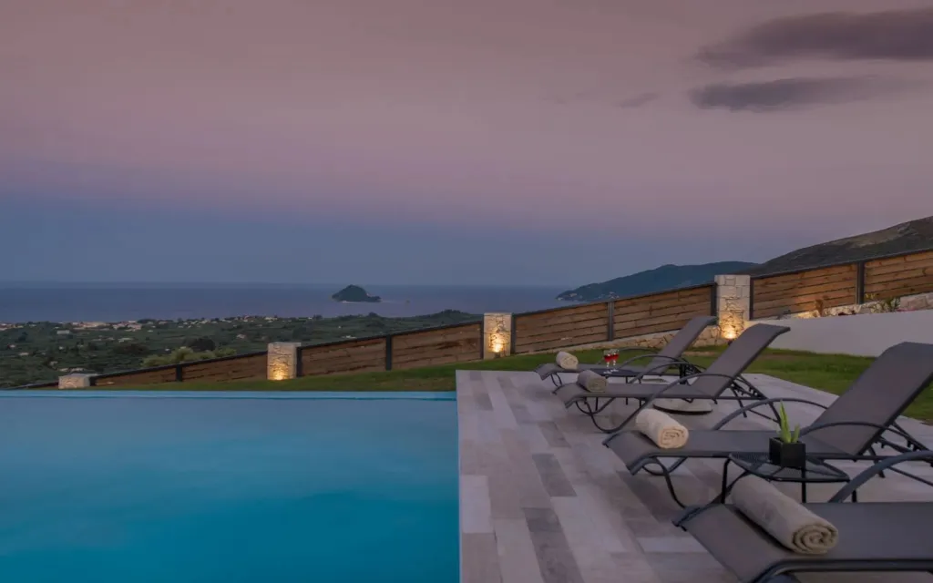 Transats alignés au bord d'une piscine avec vue sur la mer au coucher du soleil.