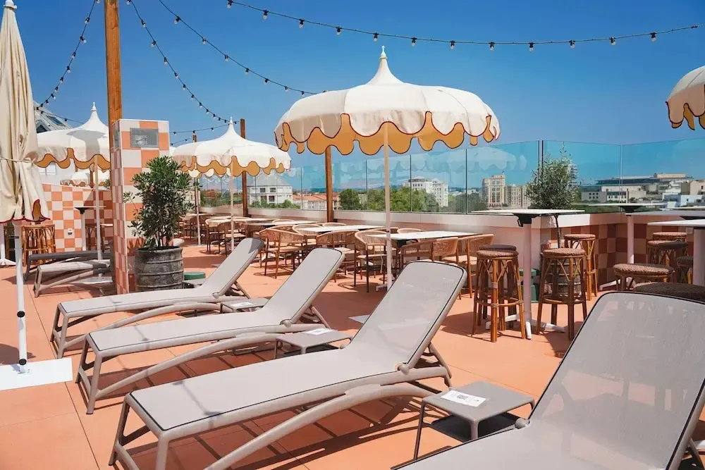 Terrasse aménagée avec transats et tables ombragées offrant une vue sur la ville.