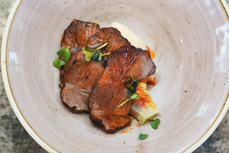 Assiette de viande tranchée accompagnée d'une purée et d'une garniture verte.