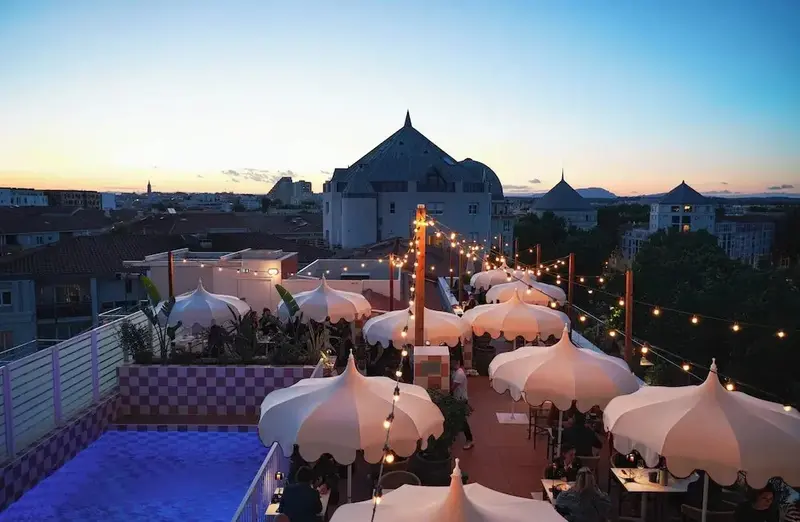 Terrasse aménagée avec parasols et vue sur la ville au coucher du soleil.