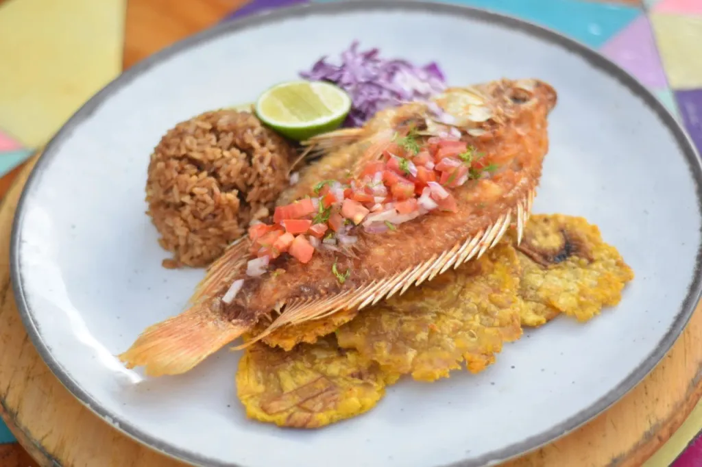 Assiette de poisson frit servi avec du riz, des bananes plantains et une salade de chou.