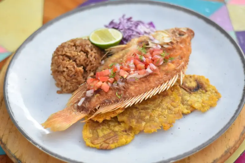 Assiette de poisson frit servi avec du riz, des bananes plantains et une salade de chou.