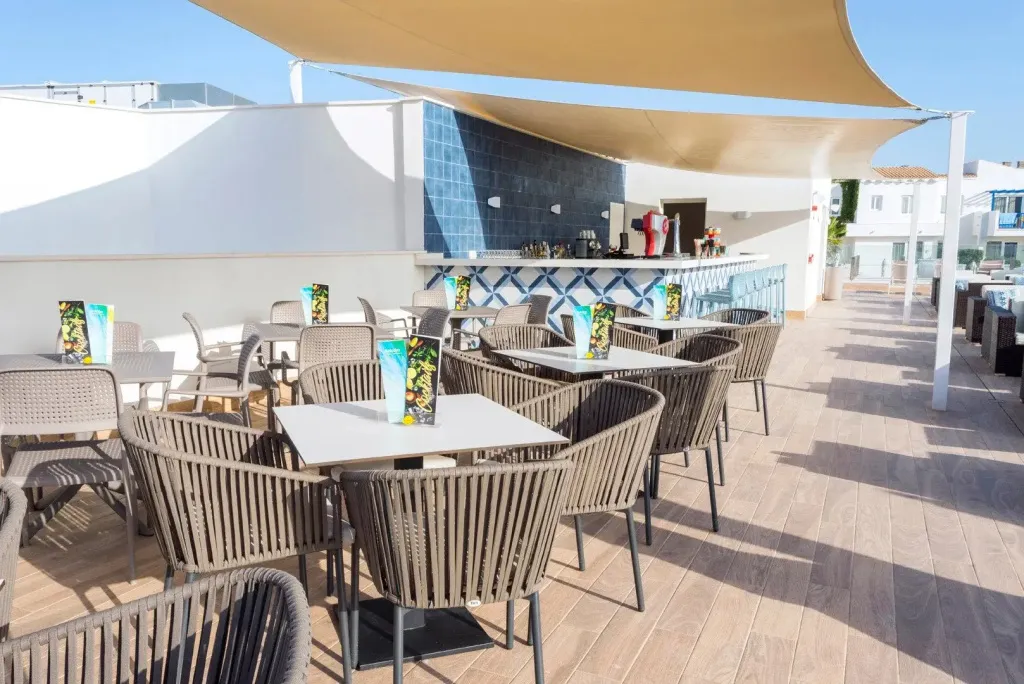 Terrasse ombragée avec tables et comptoir de bar.