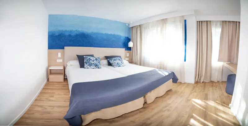 Une chambre lumineuse avec un grand lit et un mur décoratif bleu.