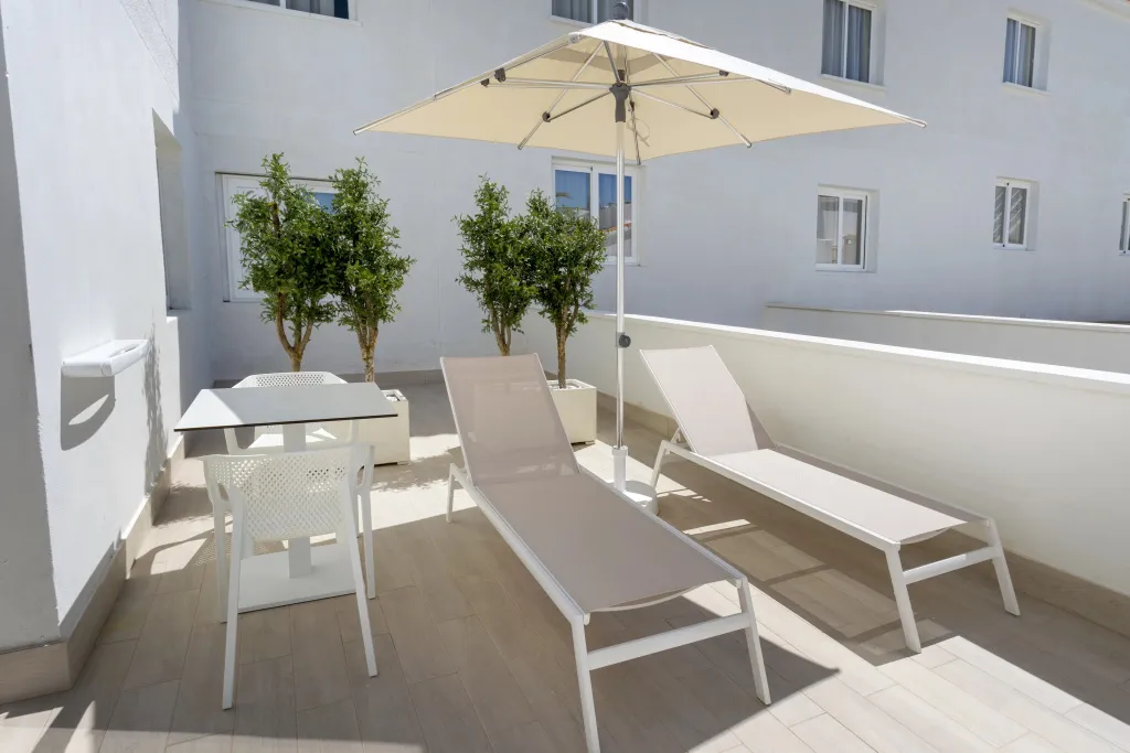 Terrasse aménagée avec table, chaises et transats à l'ombre d'un parasol.