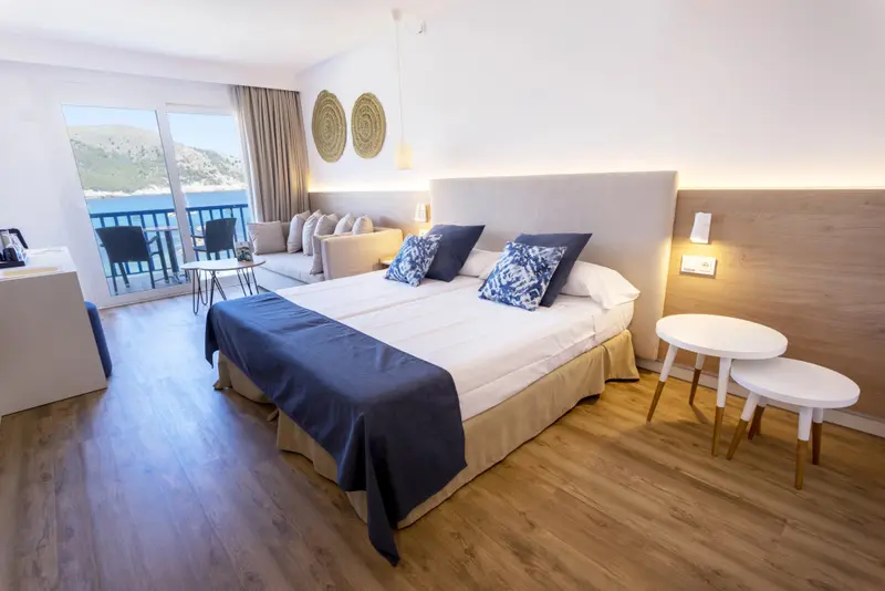 Une chambre lumineuse avec un grand lit et un coin salon donnant sur la mer.