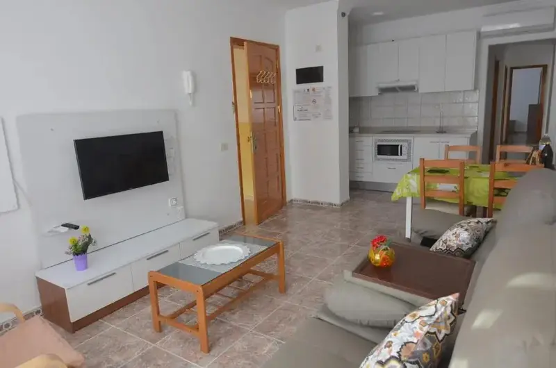 Un espace de vie lumineux avec un canapé, une table basse et un téléviseur mural.