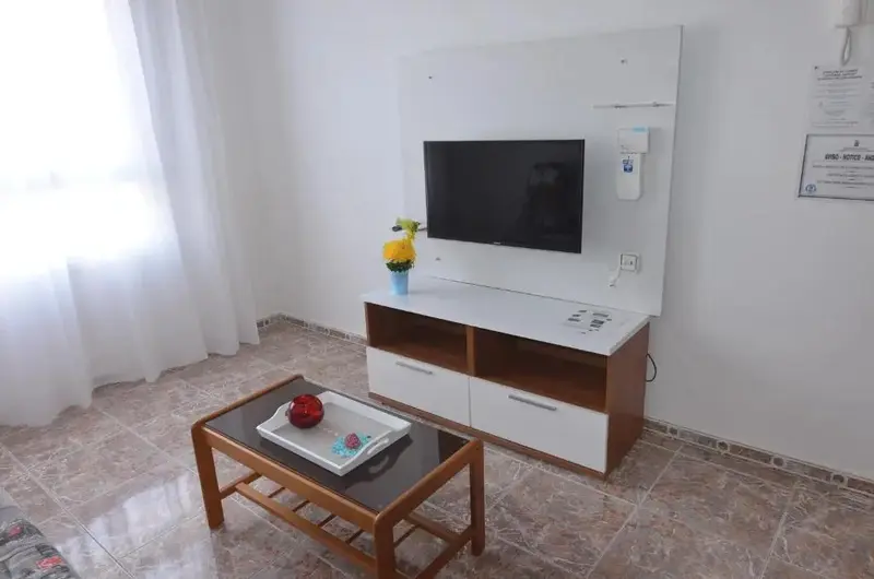 Un salon lumineux avec un téléviseur fixé au mur et une table basse.