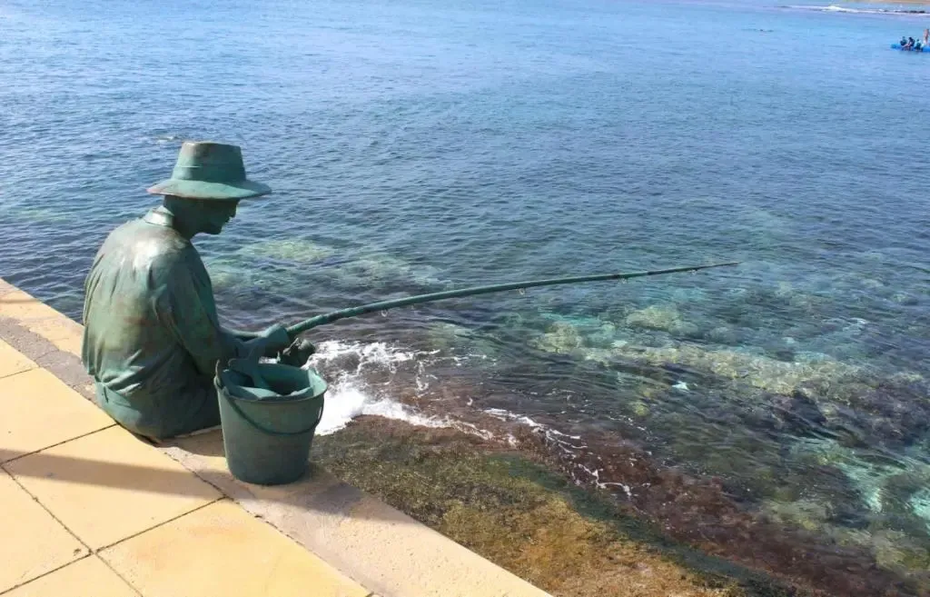 Une statue de pêcheur est assise au bord de l'eau.