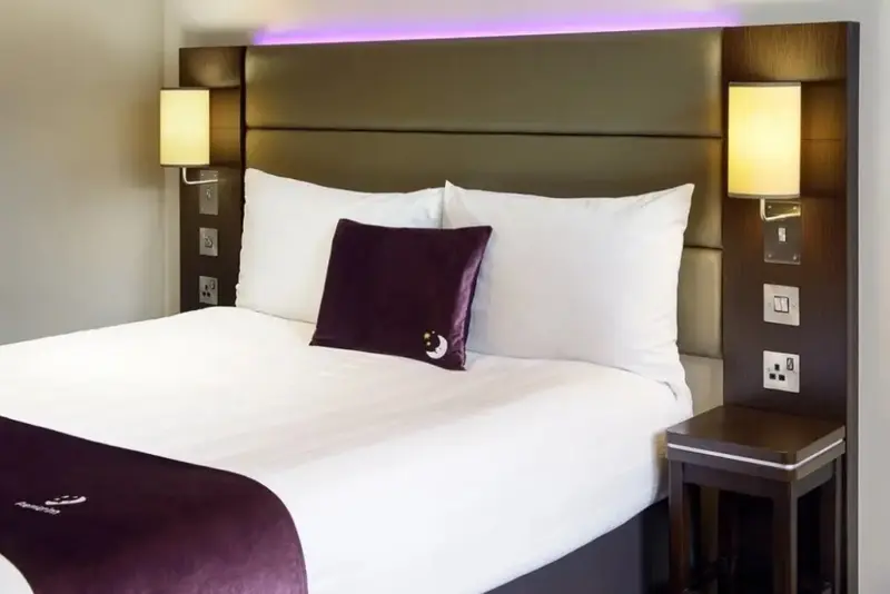 Un lit double avec des oreillers blancs et un coussin violet foncé dans une chambre d'hôtel.