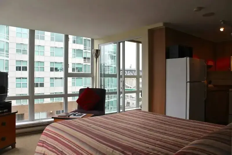 Une chambre avec un grand lit donnant sur une vue urbaine à travers de larges fenêtres.