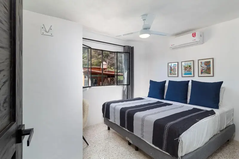Une chambre lumineuse avec un grand lit recouvert d'une couette rayée et des coussins bleus.