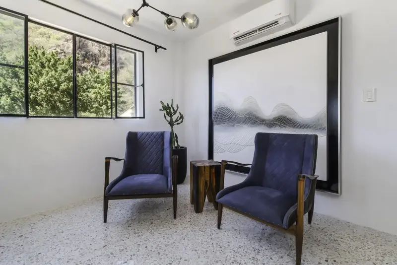 Deux fauteuils bleus sont placés devant une grande fenêtre et un tableau abstrait.