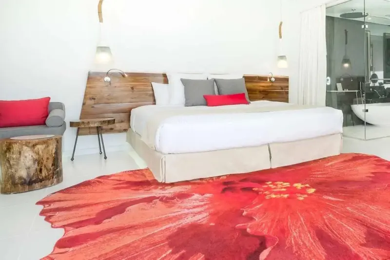 Une chambre lumineuse avec un grand lit et un tapis rouge vif.