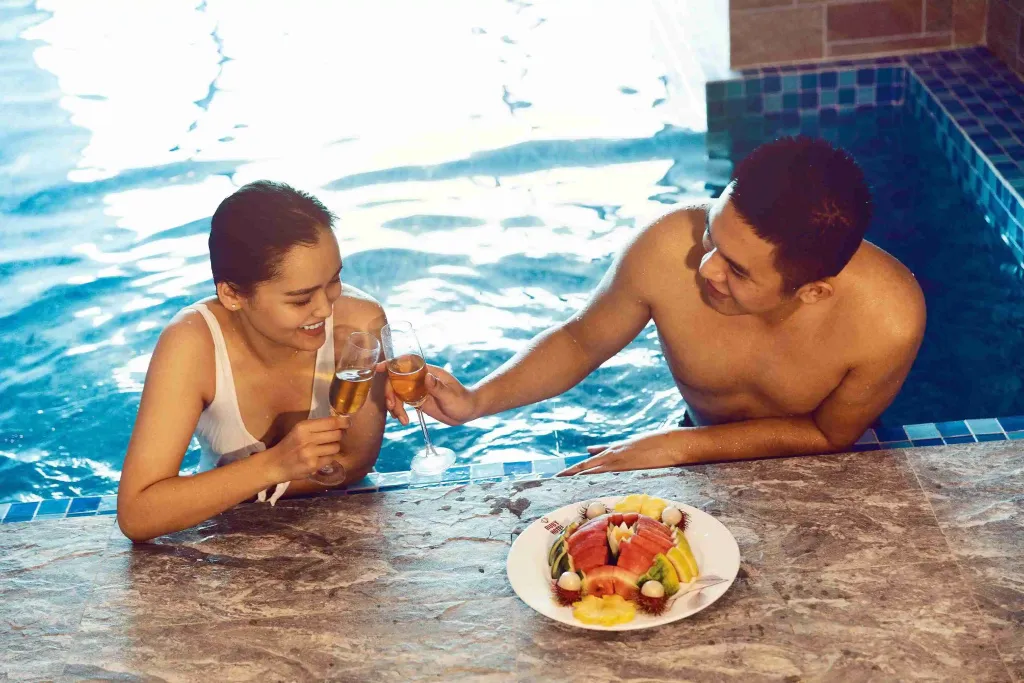 Un couple rit en sirotant des boissons au bord d'une piscine.