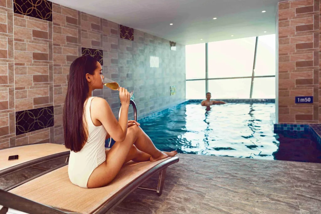 Une femme se détend au bord d'une piscine intérieure avec une boisson.