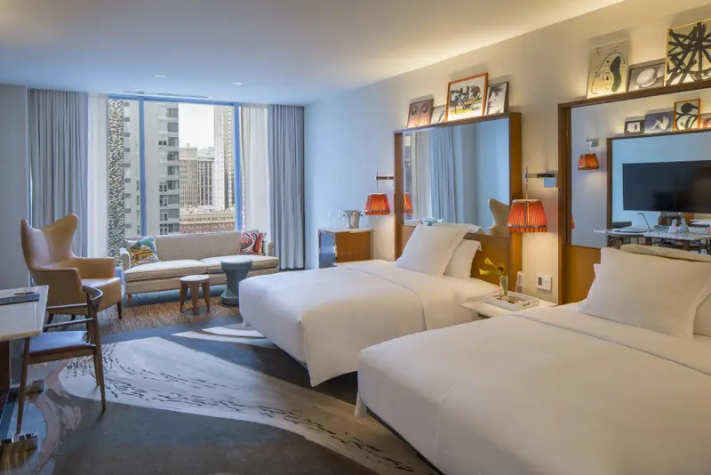 Une chambre lumineuse avec deux lits et un coin salon près d'une fenêtre.