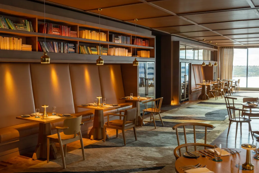 Une salle de restaurant lumineuse avec des tables dressées et une bibliothèque murale.