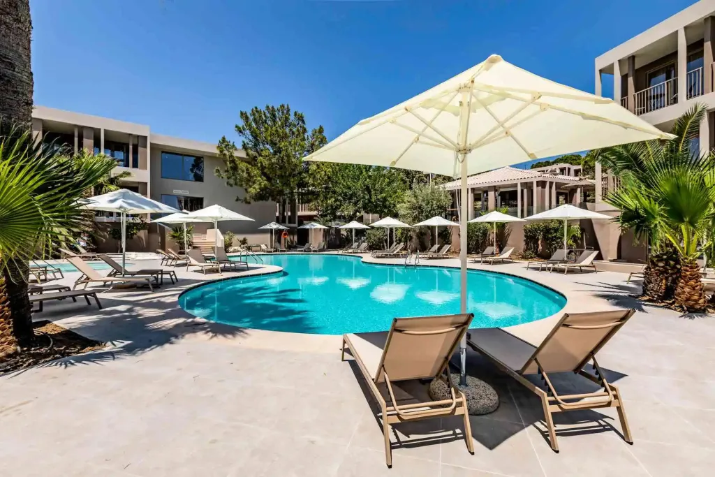 Transats et parasols bordent une piscine rectangulaire dans un espace extérieur ensoleillé.