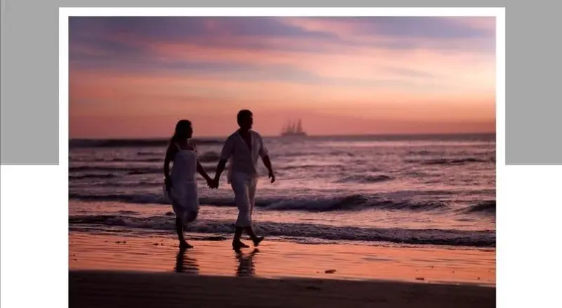 Un couple se promène main dans la main sur une plage au coucher du soleil.