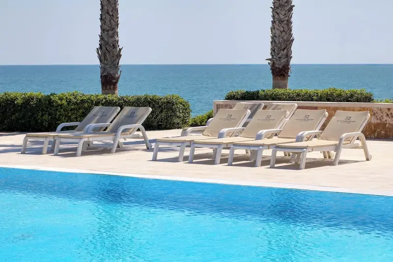 Transats alignés au bord d'une piscine turquoise avec vue sur la mer.