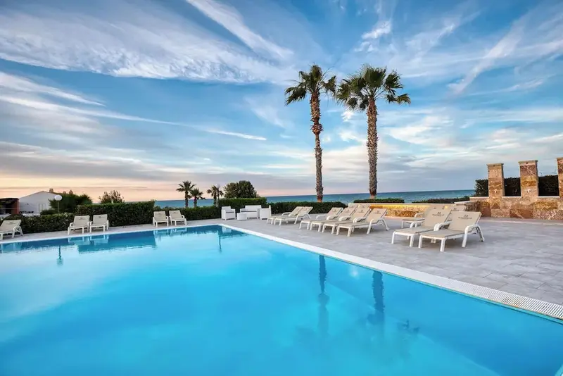 Une piscine turquoise reflète le ciel nuageux et les palmiers environnants.