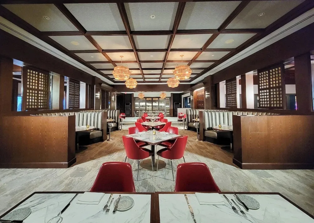 Une salle de restaurant lumineuse avec des tables dressées et des banquettes rouges.