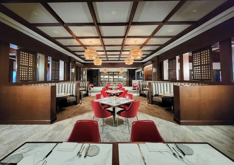 Une salle de restaurant lumineuse avec des tables dressées et des banquettes rouges.